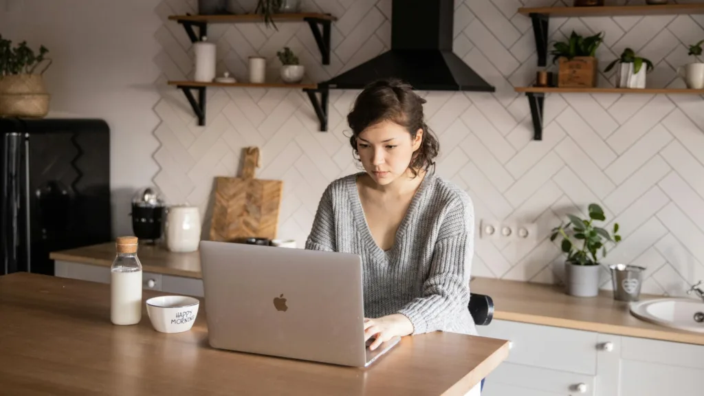Young woman sitting at kitchen table using laptop, searching for a local mental health therapist online
