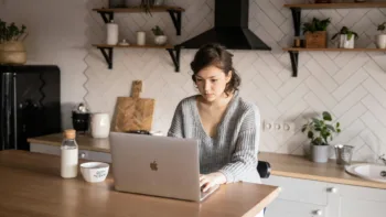 Young woman sitting at kitchen table using laptop, searching for a local mental health therapist online