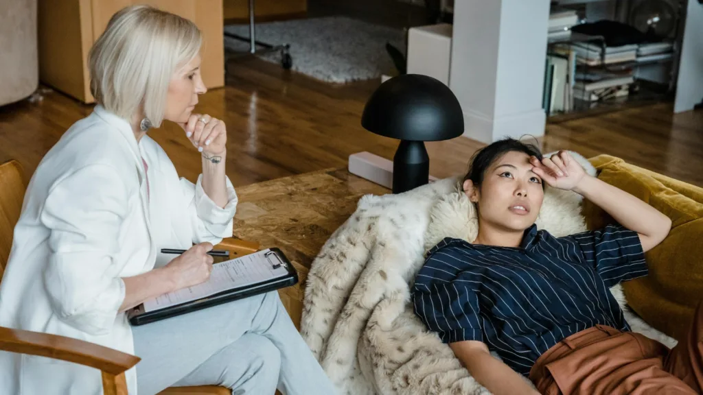 Therapist taking notes while woman lies back on couch, appearing emotionally exhausted during a counseling session