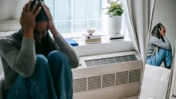Woman sitting with her head in her hands, reflecting emotional distress and internal conflict, mirrored in her reflection