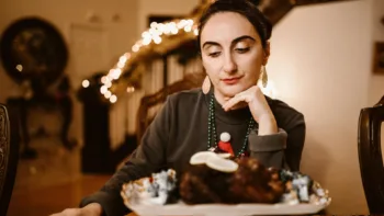 Woman sitting at a holiday table, reflecting quietly as she prepares to set boundaries during the festive season